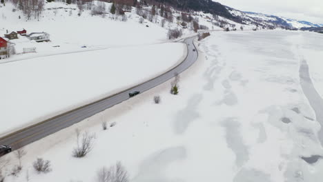 cars driving on winding road near small village and snowy fields at wintertime in haugastol, norway