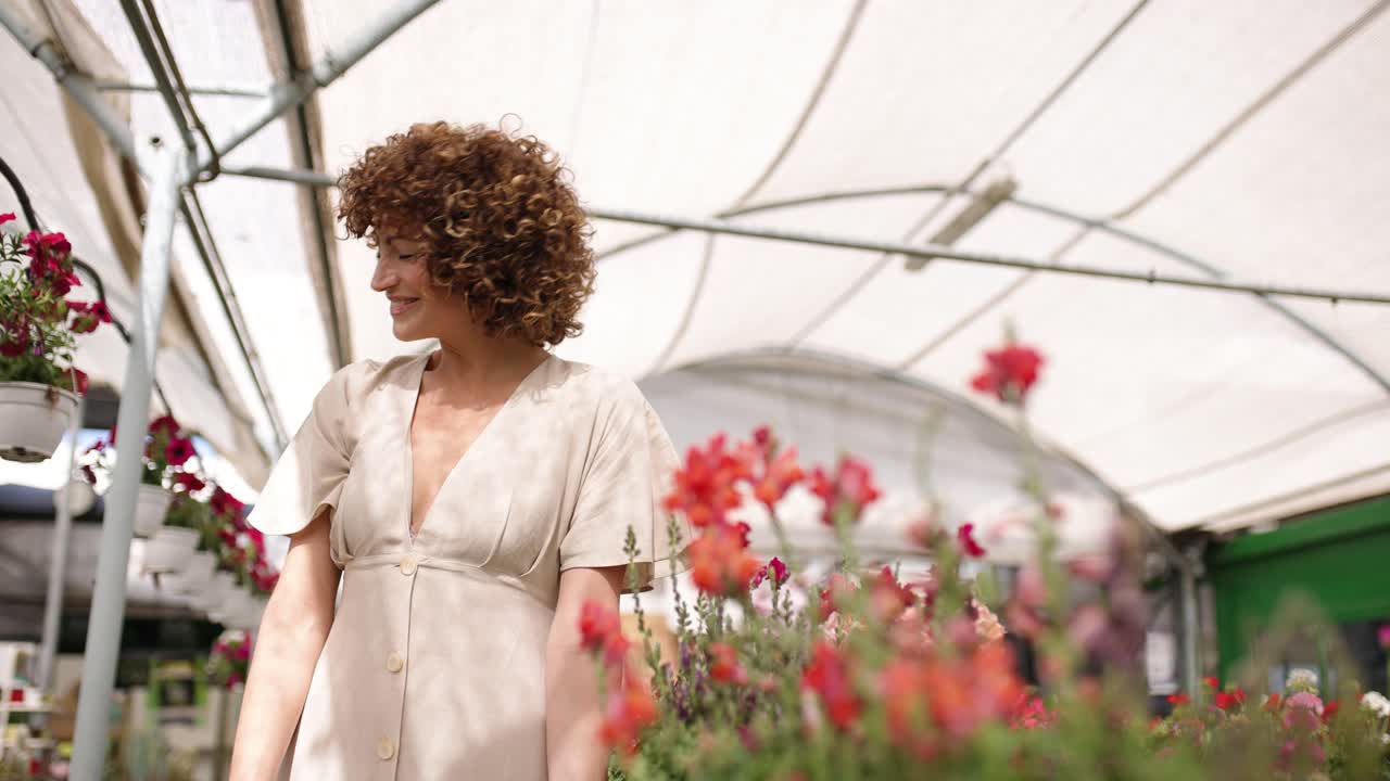 Young women smelling blooming flowers inside greenhouse nursery
