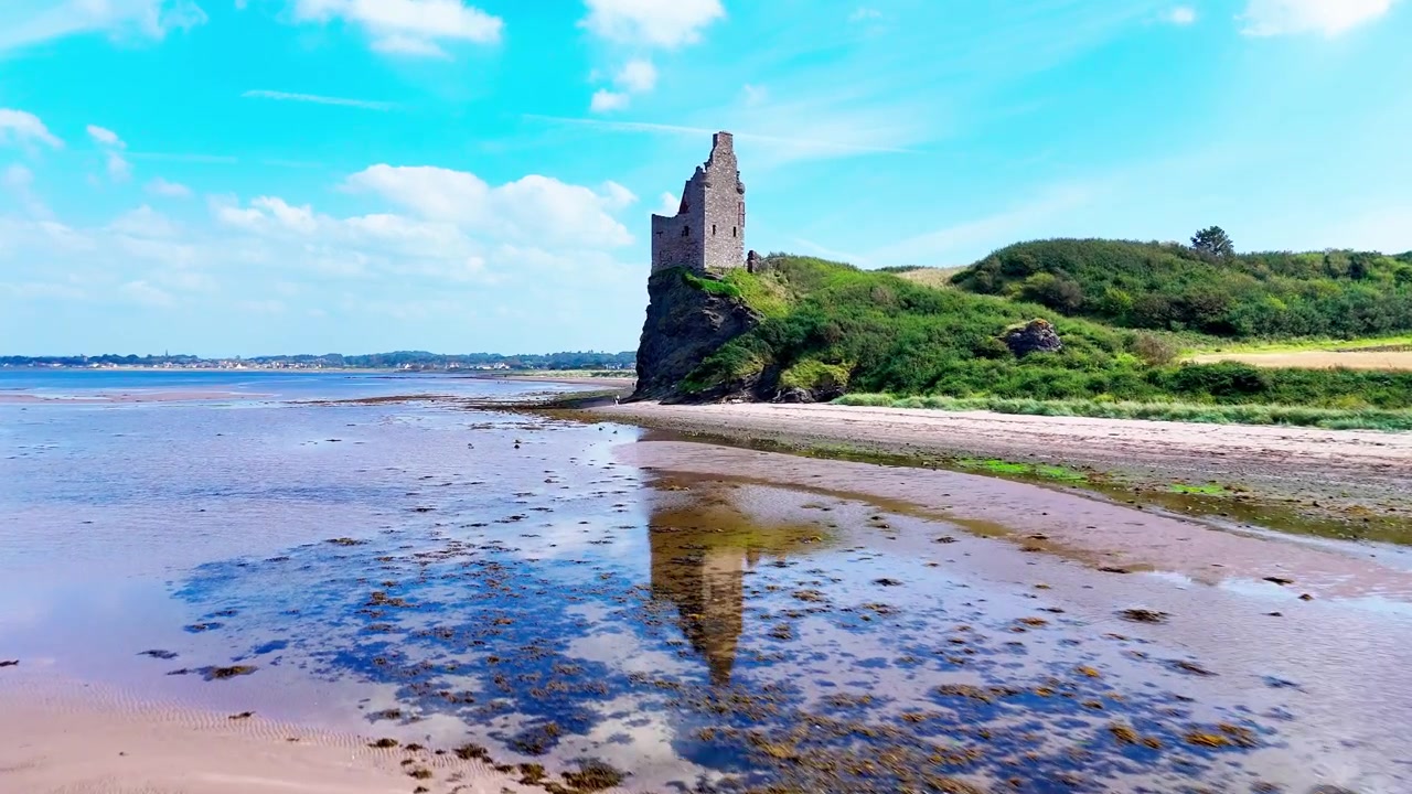 Greenan Castle ad Ayr, in Scozia, che mostra lo storico rudere costiero sopra una spiaggia sabbiosa, terreni agricoli e il Firth of Clyde, ripresa aerea con movimento in avanti