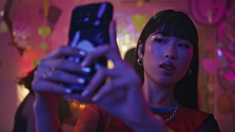 party girl capturing selfie on cellphone at vibrant neon nightlife closeup