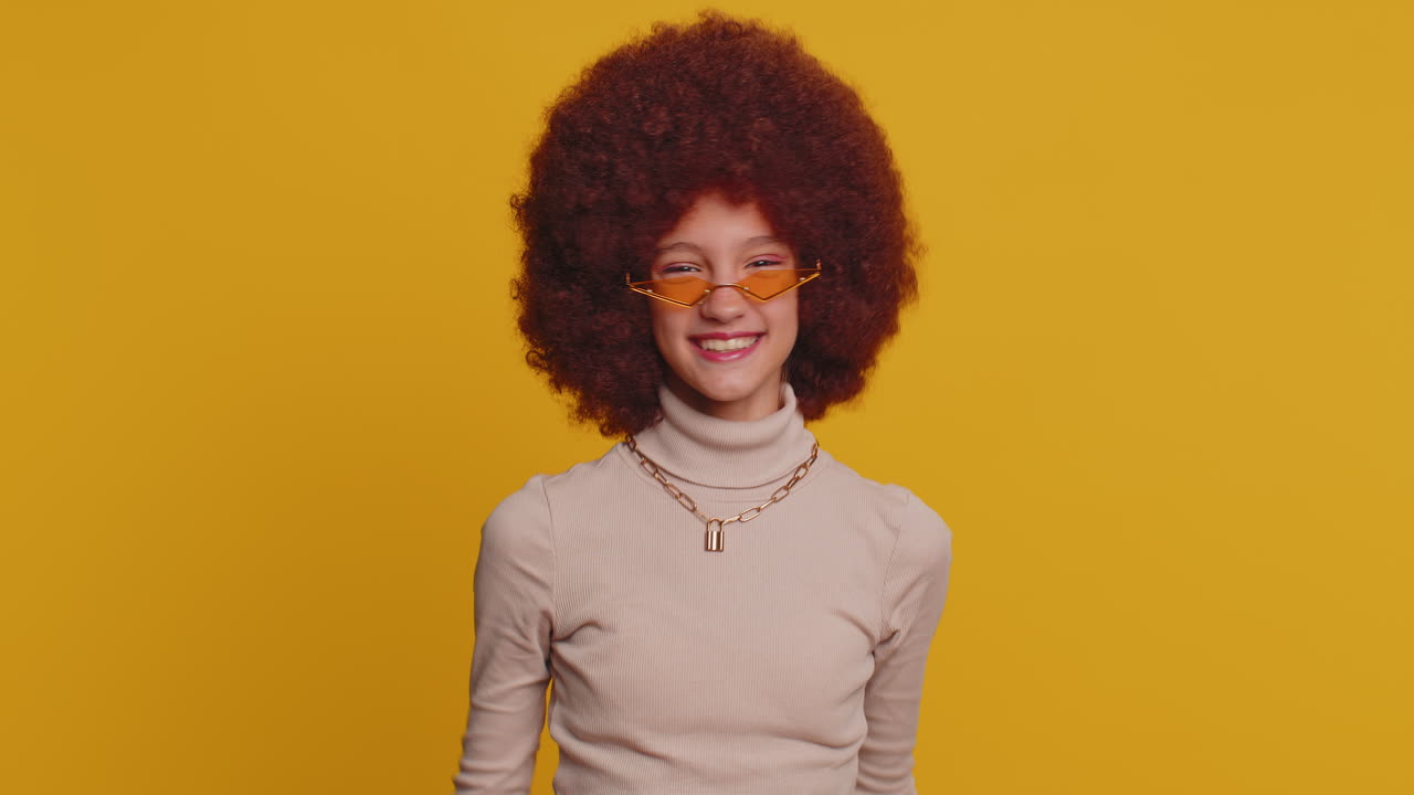 joven chica de escuela divertida niño sonriendo amistoso gesticulando hola o adiós, bienvenida, agitando las manos