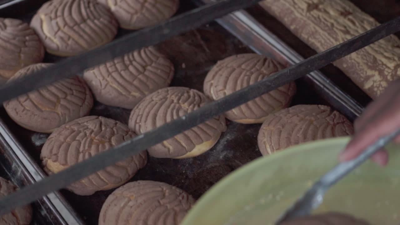una persona usa pinzas para agarrar un pastel recién horneado de una hoja de hornear en una panadería