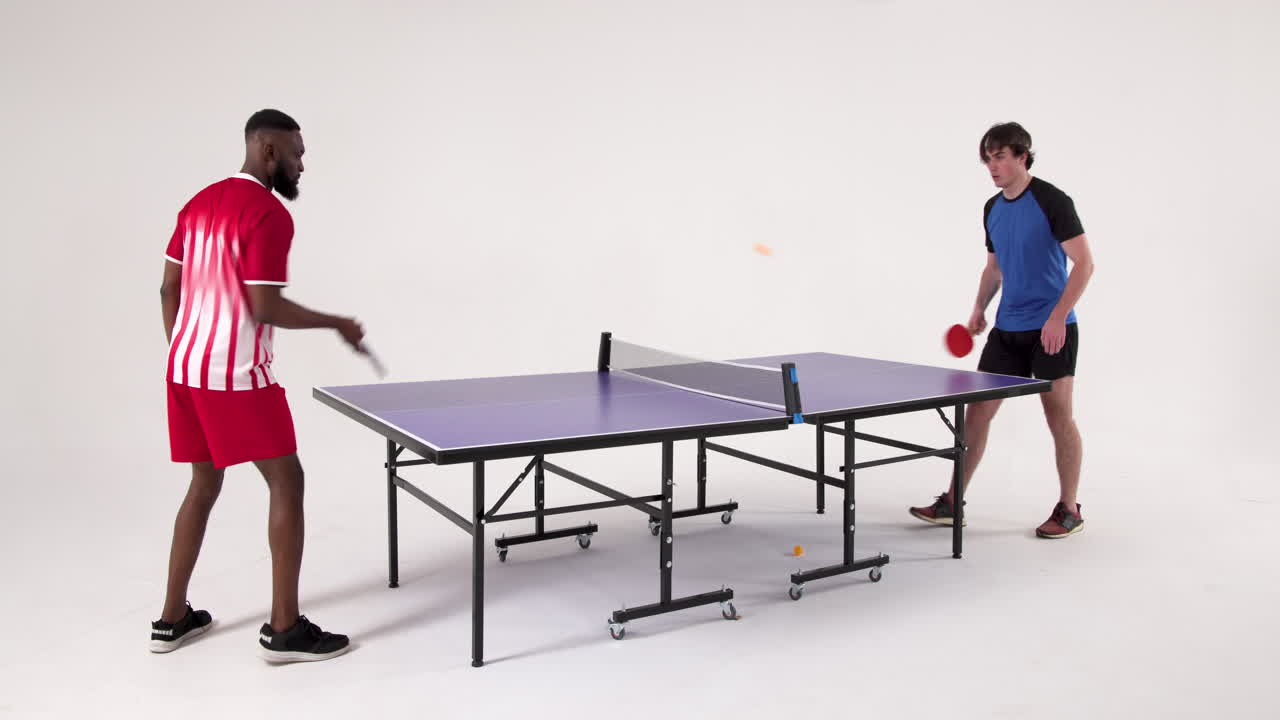 Competing in table tennis, two men playing intensely in studio setting