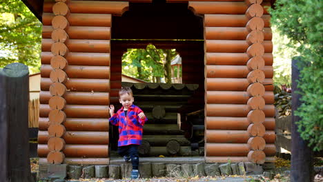 caucasian toddler in checkered shirt stands in the wooden alcove. happy smiling baby runs up to camera.
