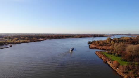 Vista-Aérea-Sobre-El-Paisaje-Otoñal-Junto-A-Oude-Maas-Con-El-Barco-Pasando-En-Segundo-Plano