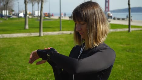 young sportswoman standing on lawn and checking smartwatch