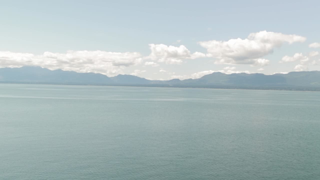 캐나다 브리티시 컬럼비아에 있는 혼비 섬의 바다 바로 너머 배경에 있는 록키 산맥을 응시하는 헬리웰 초원의 절벽 가장자리에 서 있습니다.