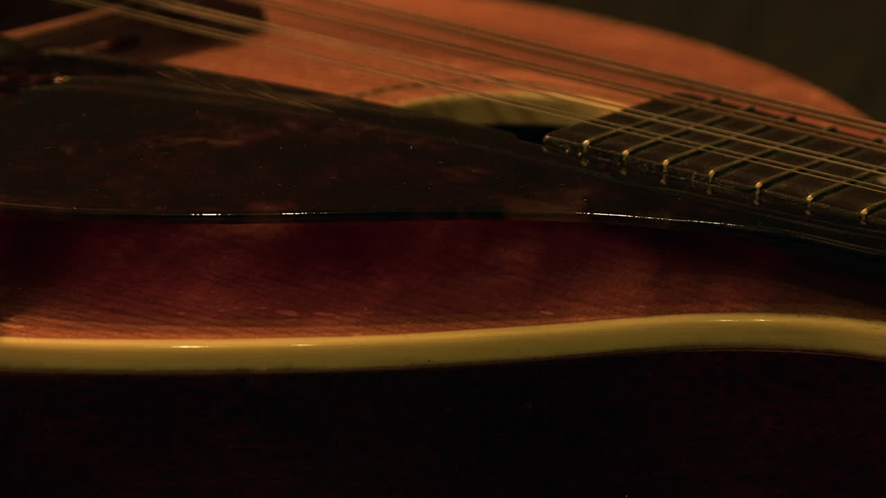 Primo piano: Mandolino Gibson vintage che ruota nella luce fioca della stanza, musicale.