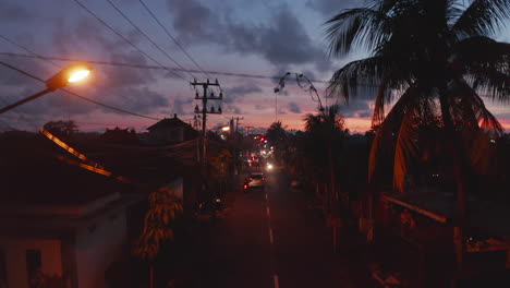Vista-De-La-Calle-Del-Tráfico-De-La-Ciudad-En-Las-Calles-Tropicales-De-Bali-Durante-La-Puesta-De-Sol.-Vista-Aérea-Ascendente-Del-Tráfico-En-Las-Calles-De-Indonesia-Por-La-Noche