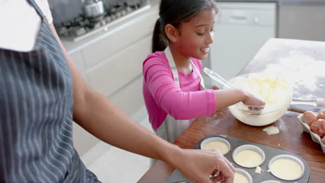 Feliz-Hija-Birracial-Probando-Mezcla-De-Pastel,-Horneando-Con-Madre-En-La-Cocina,-Cámara-Lenta