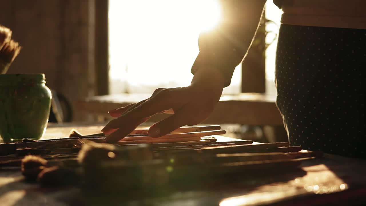 imágenes de cerca de una mano femenina cuidadosamente manicurada dudando en elegir un pincel de una fila en la mesa.