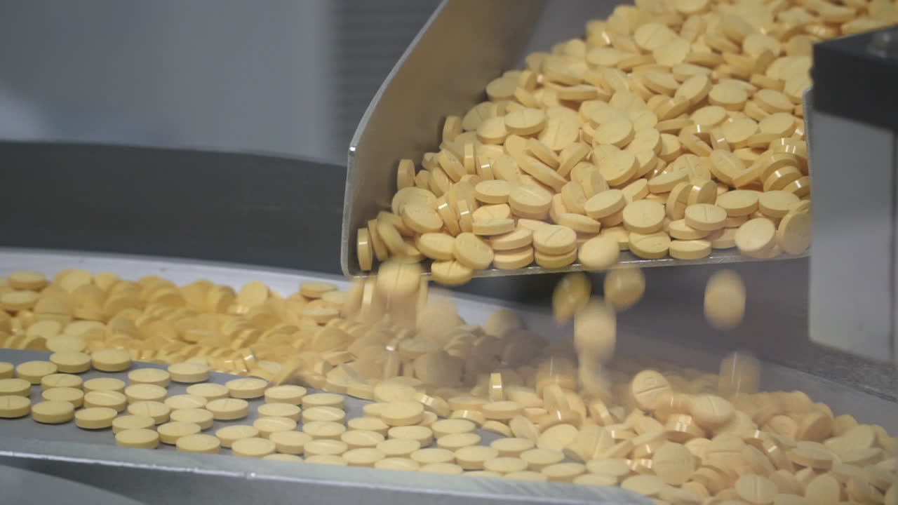 Pharma lab machine drops round yellow drug pills into rotational platform, close up