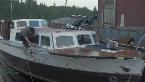 young man carpenter cleaning edge of waterproof sealant windows wooden boat