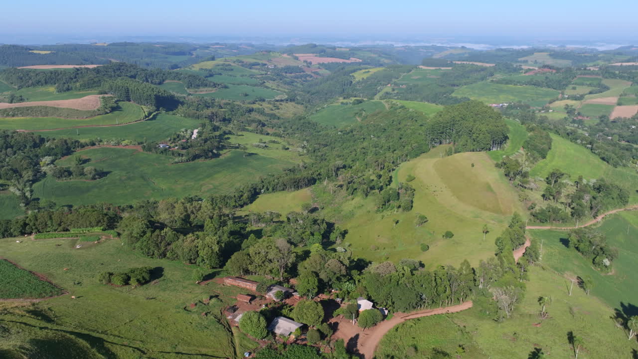 Panorama aereo con drone su terreni agricoli misti, macchie di foresta, strade rurali e dolci colline.