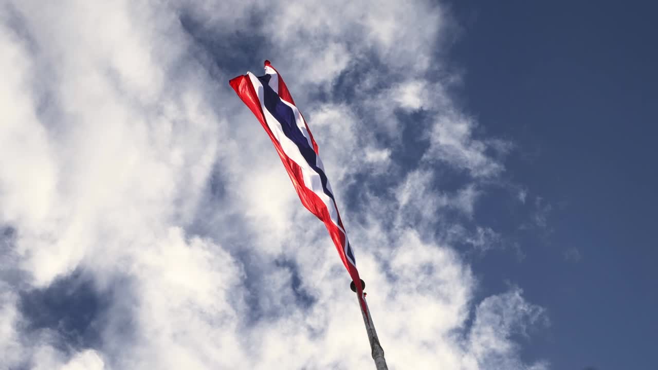 Bandiera del Regno di Thailandia che sventola su un'asta con cielo blu e nuvole bianche sullo sfondo.