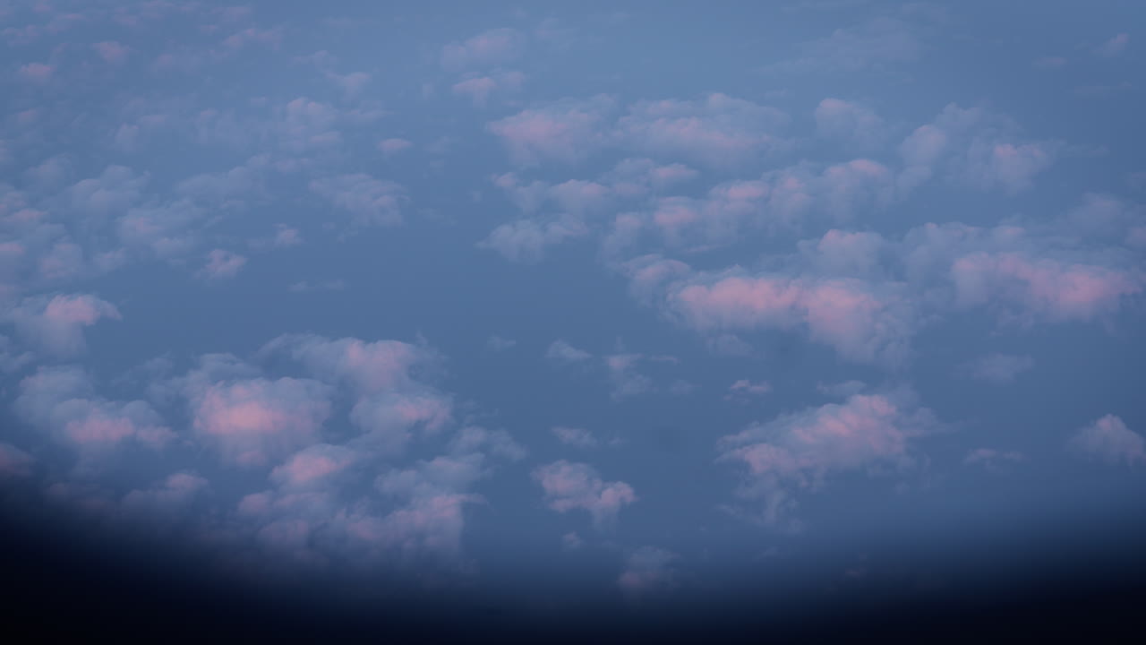 A stunning view of the sunset seen through an airplane window, with soft pastel clouds floating below. This tranquil aerial scene captures the beauty of flying above the clouds during golden hour