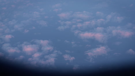 a stunning view of the sunset seen through an airplane window, with soft pastel clouds floating below. this tranquil aerial scene captures the beauty of flying above the clouds during golden hour