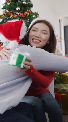 video vertical de una feliz pareja diversa intercambiando regalos de navidad y abrazándose en casa