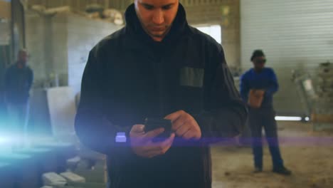 animation of glowing light over caucasian man using smartphone working in factory