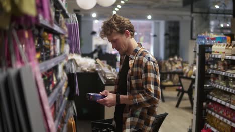 customer in the supermarket. man choosing, picking the pack of the coffee. shelves on the background. side view