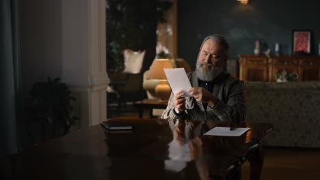 elderly man opening envelope with knife in ancient cabinet. old man