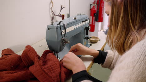 wide shot of caucasian seamstress sewing red fabric with a sewing machine