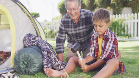 Happy-caucasian-grandfather-and-grandson-pitching-tent-together-in-garden,-slow-motion