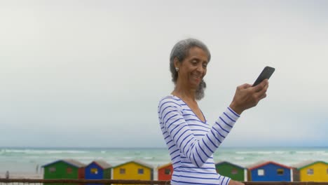 Side-view-of-active-senior-African-American-woman-talking-selfie-with-mobile-phone-on-promenade-4k