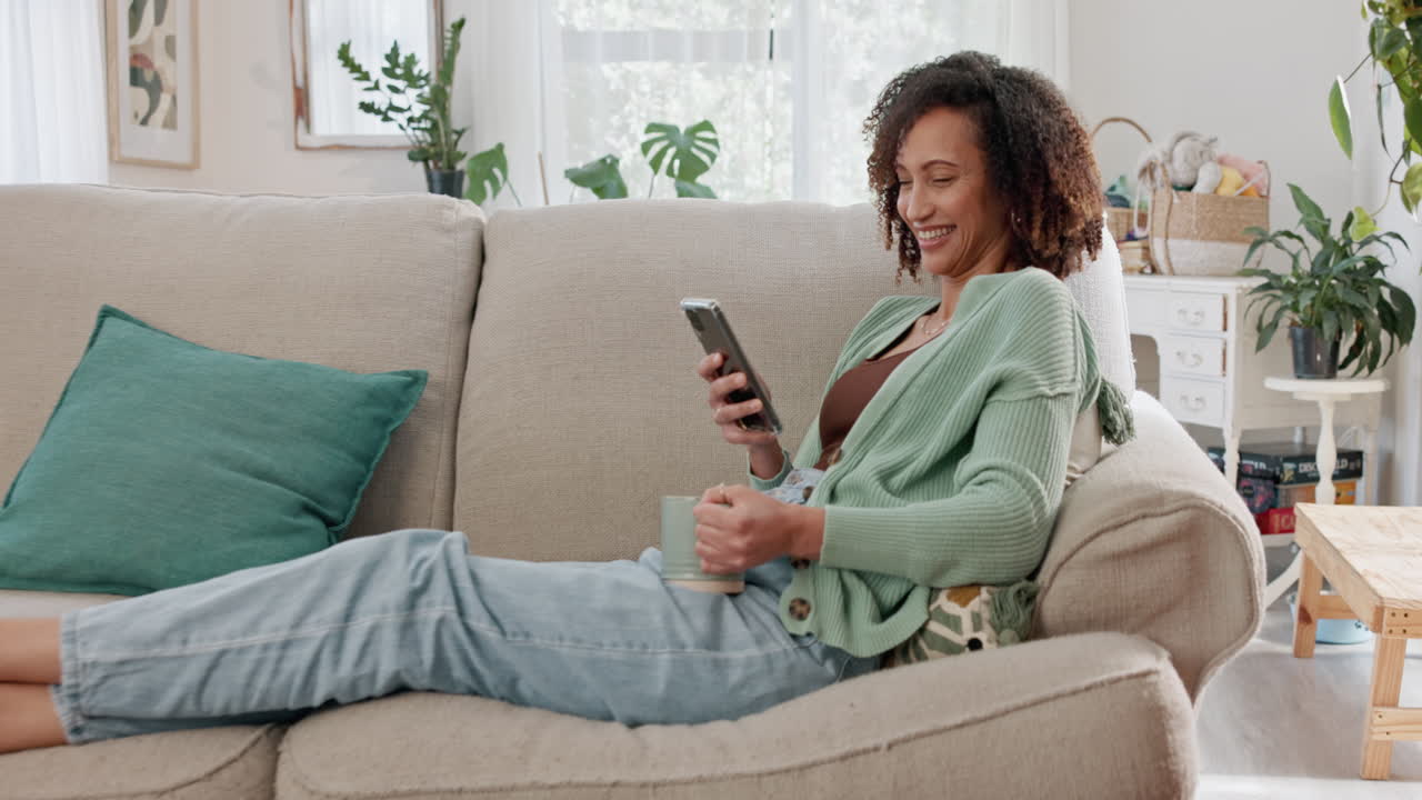 mujer feliz riendo mientras mira su teléfono en el sofá