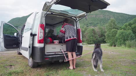 caucasian man and his pet alaskan malamute camping with packed things at the back of minivan