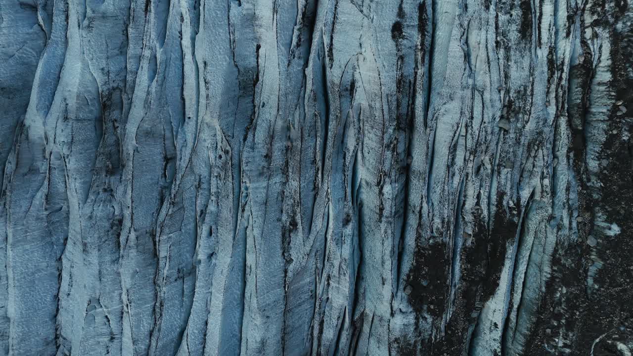 Blaue Gletschereisoberfläche mit dunklen Gletscherspalten und strukturierten Mustern in Norwegen, Top-Down-Drohnen-Nahaufnahme.