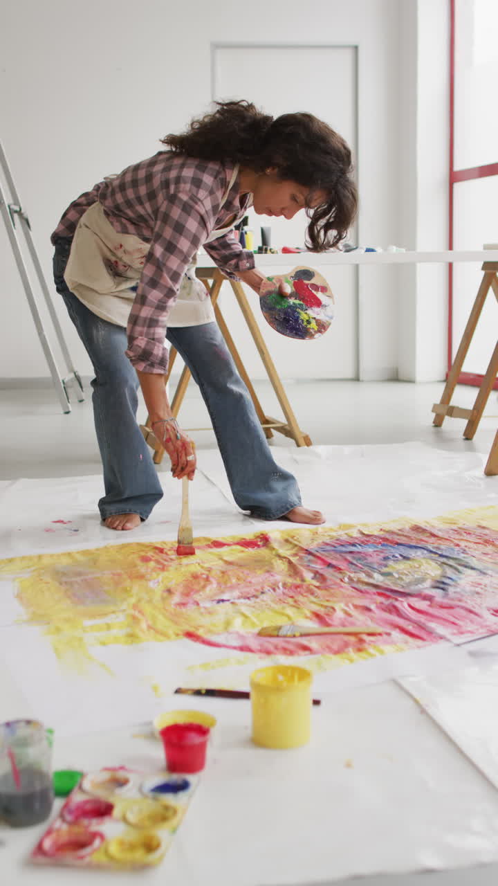 video vertical de una artista femenina biracial pintando en el suelo en el estudio