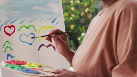 portrait of senior african american woman painting while standing on the porch of the house