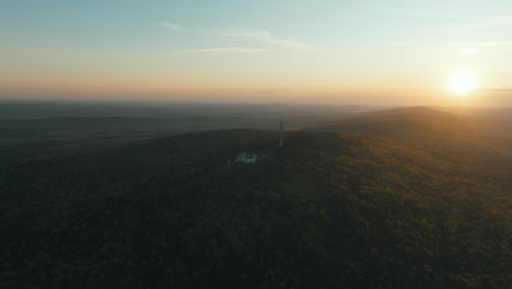 sunset over a hilltop with forest and building