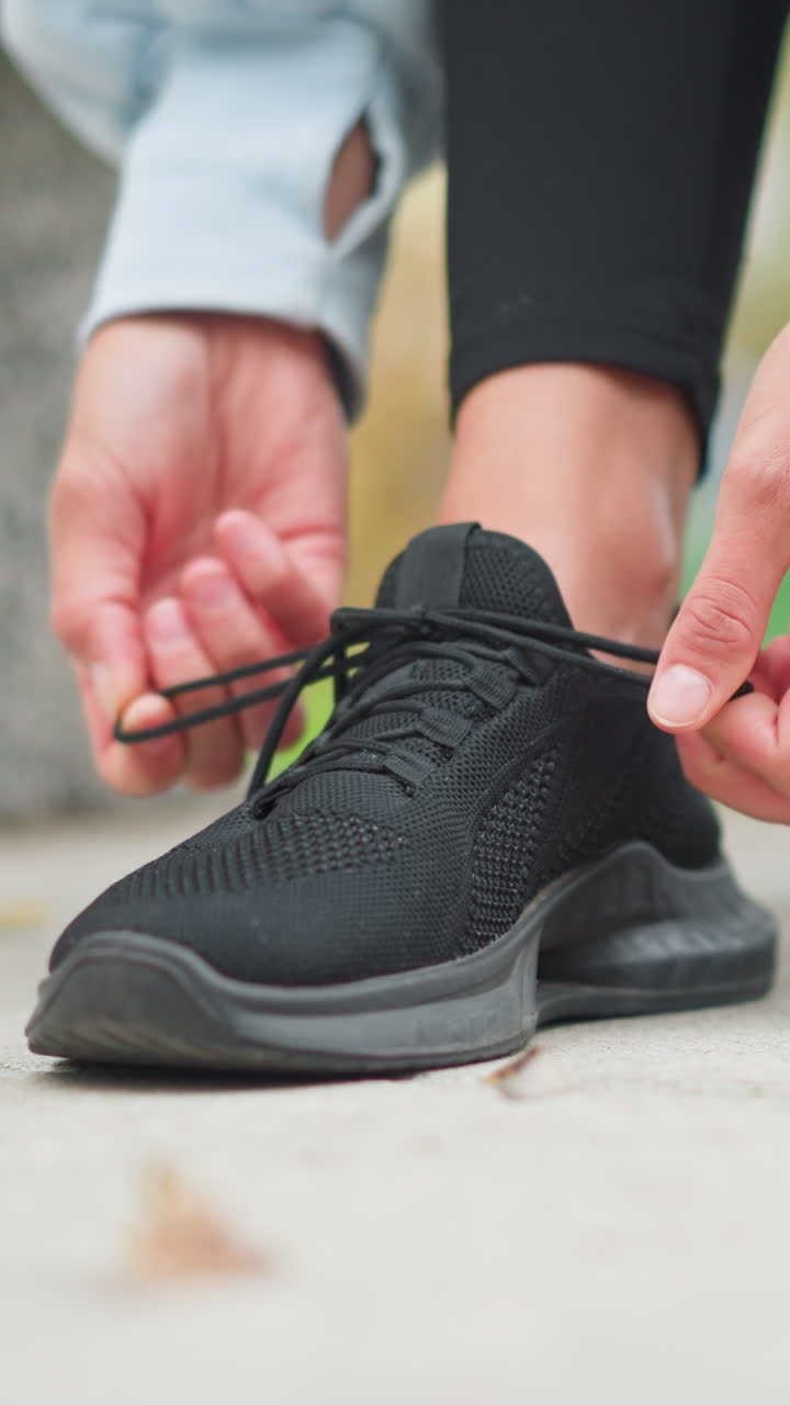 Close-up of sport fair lady tightening one of her black sneaker shoelaces, wearing rings on both hands, preparing for workout, focused on footwear and active lifestyle, ready for exercise