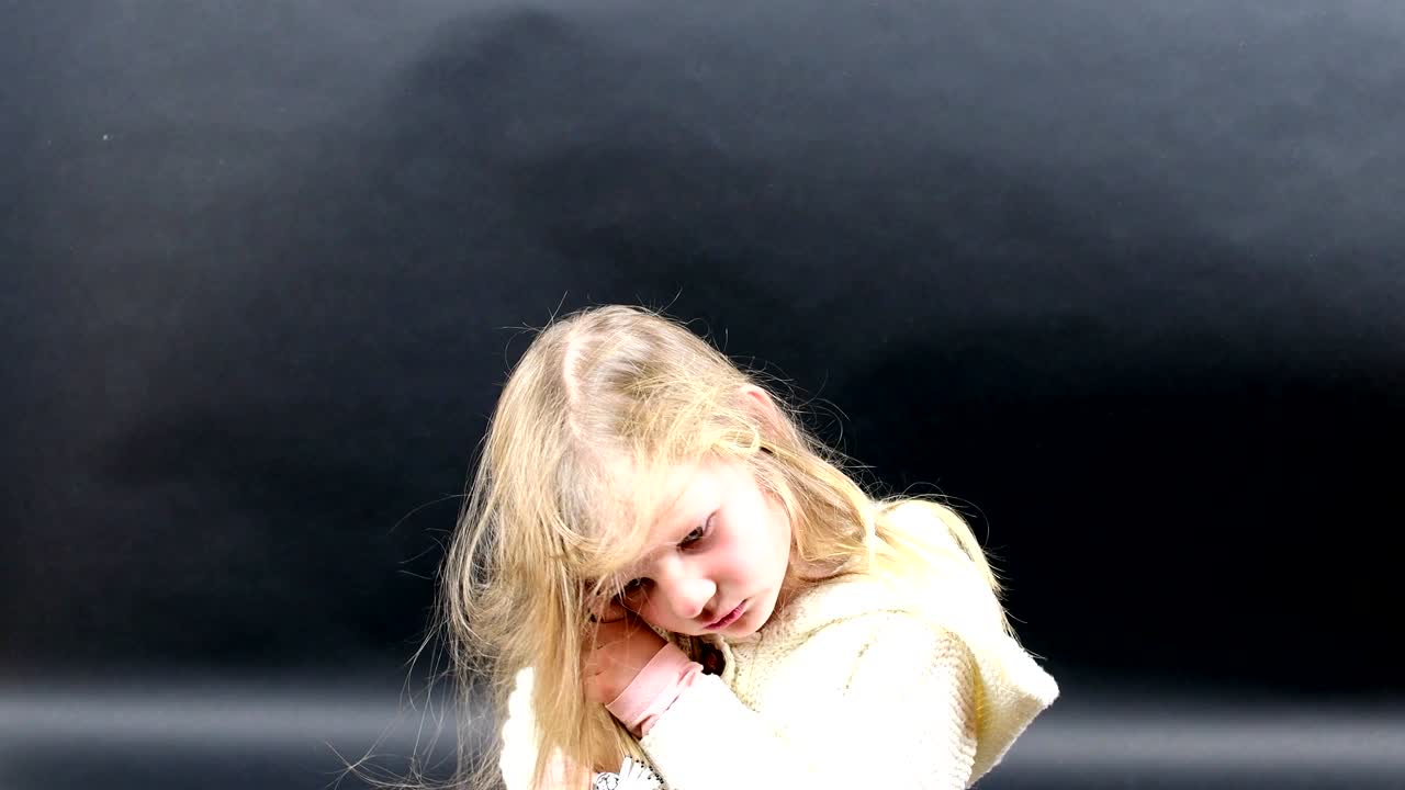 Una bambina carina si pettina i capelli. La bambina è vestita con abiti invernali. Carina bambina su sfondo nero.