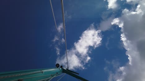 a shot from below of a mast, with a background of blue sky and cotton clouds