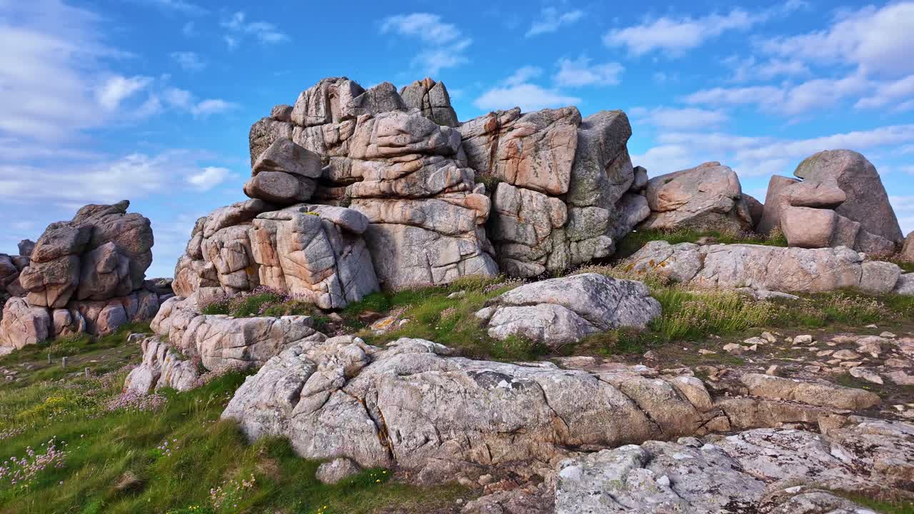Forward panning view of the rocky coast at Plougrescant in Brittany, with rugged rocks, green vegetation, and a bright blue sky - France
