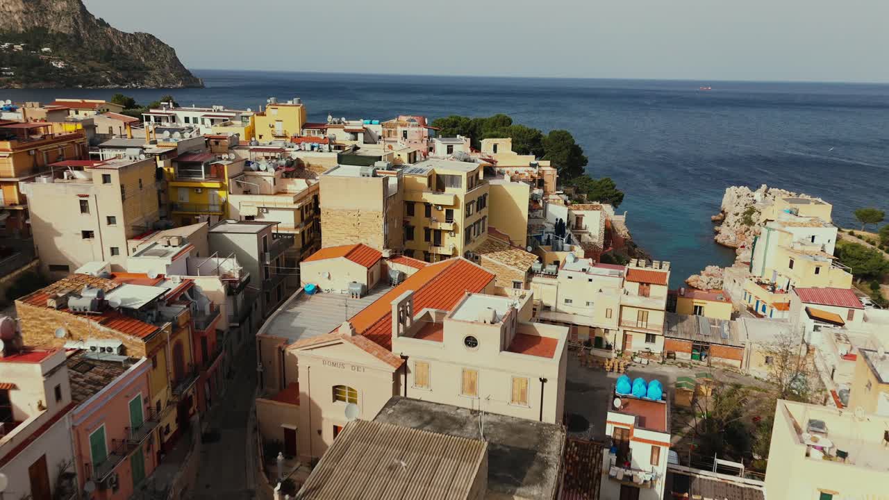 Aerial drone clip over Porticello, Sicily, showing tightly built residential rooftops, scaffolding and a view of the coastline and deep blue Tyrrhenian Sea in the background