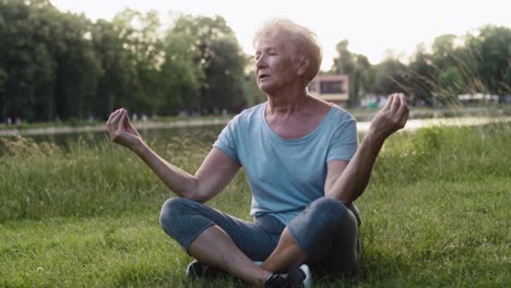 Mujer-Mayor-Tranquila-Meditando-En-El-Parque-Junto-Al-Lago