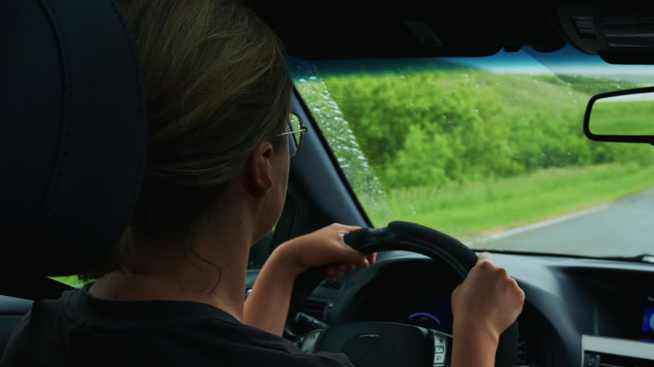 Donna alla guida di un'auto con i tergicristalli che puliscono la pioggia dal parabrezza.