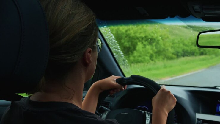 Donna alla guida di un'auto con i tergicristalli che puliscono la pioggia dal parabrezza.