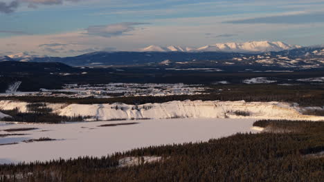 captivating aerial view of whitehorse, yukon, at golden hour. the snow-covered city and frozen yukon river glisten beneath a vibrant sunset. fish lake in the foregrond.