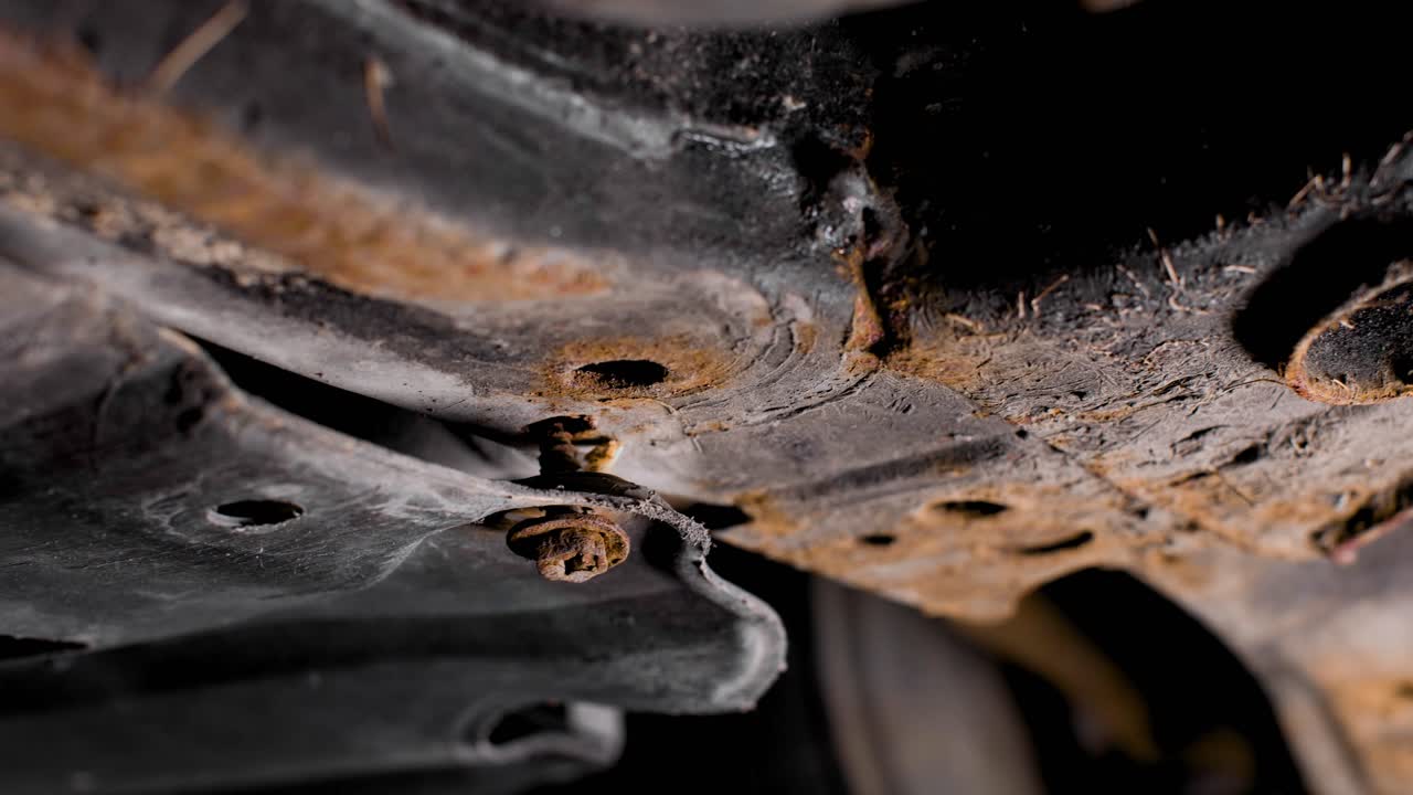 Rotating around a rusty screw hanging loose underneath a used car. 4k shot.