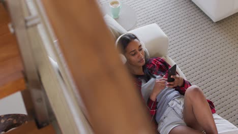 Mixed-race-woman-using-a-smartphone,-listening-to-music-with-headphones-on