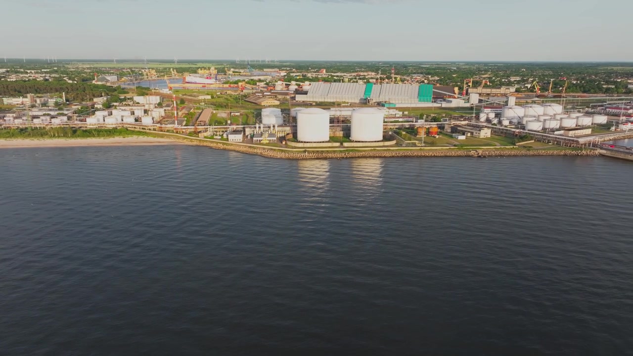 Filmato aereo fluido con drone del terminal petrolifero di Ventspils e dell'infrastruttura portuale sulla costa del Mar Baltico in Lettonia. Grandi serbatoi di stoccaggio di petrolio, impianti industriali, condotte e l'area commerciale.