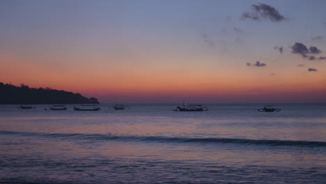 A-Medida-Que-Cae-El-Sol,-Las-Tranquilas-Aguas-De-La-Playa-De-Jimbaran-Se-Llenan-De-Siluetas-De-Barcos-Bajo-Un-Cautivador-Cielo-Azul.