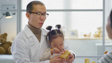 Asian Pediatrician Sitting with Little Girl and Talking to Her Mom
