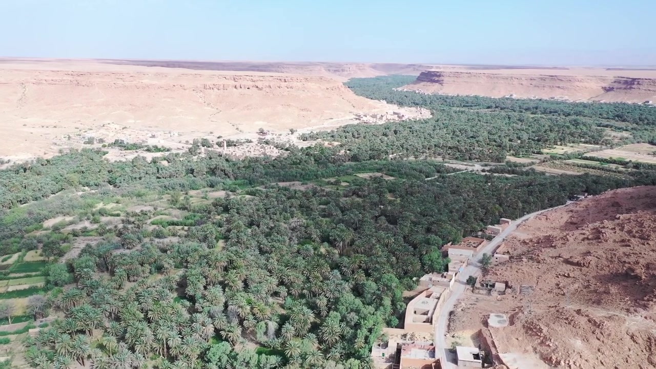 Drone aerial view of a traditional village on the edge of the Tafilalt Oasis, where date palm groves, fertile farmland, and desert plateaus define southeastern Morocco's cultural landscape.