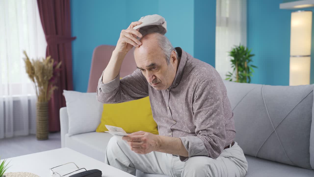 el viejo mirando la factura alta en casa está molesto.